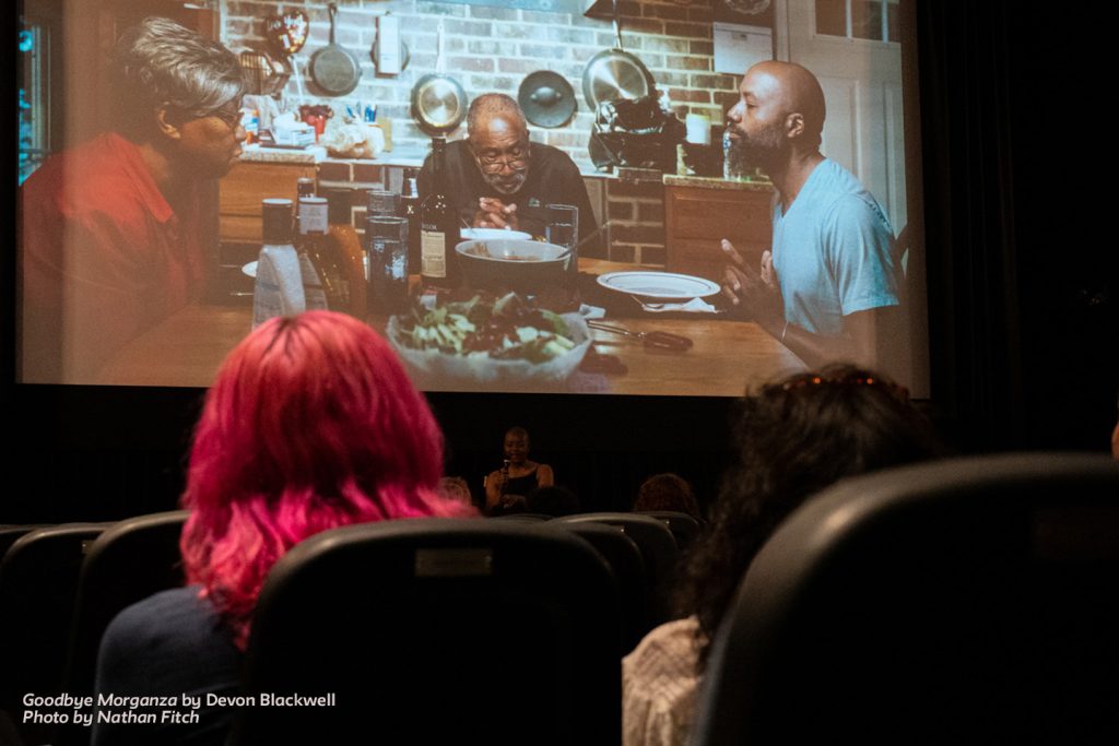 Attendees watch a scene from Goodbye, Morganza, in which three adults are having a meal at a kitchen table.