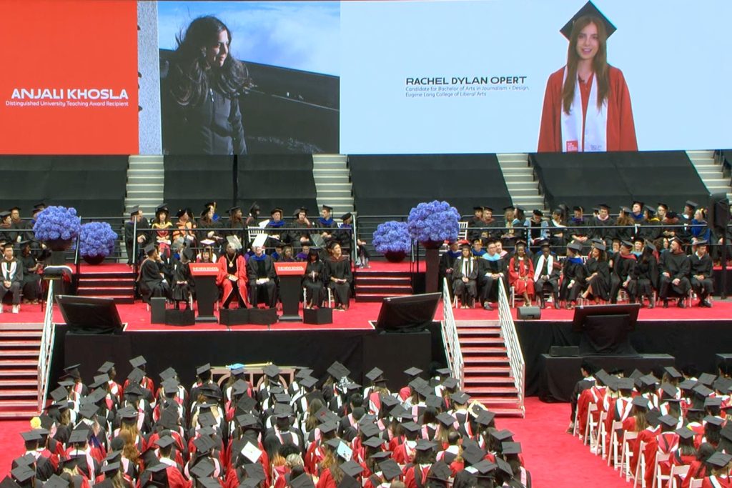 Graduates at a commencement ceremony watch a video of graduating senior introducing Anjali Khosla