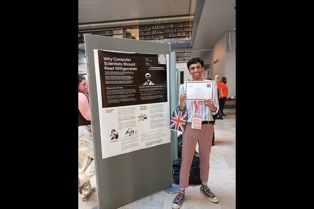 Poonamalle stands next to poster on display at conference, holding award certification.