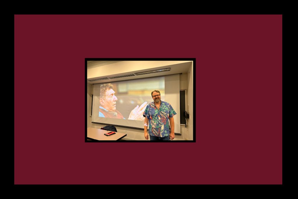 Zed Adamas stands in front of presentation at Colgate University