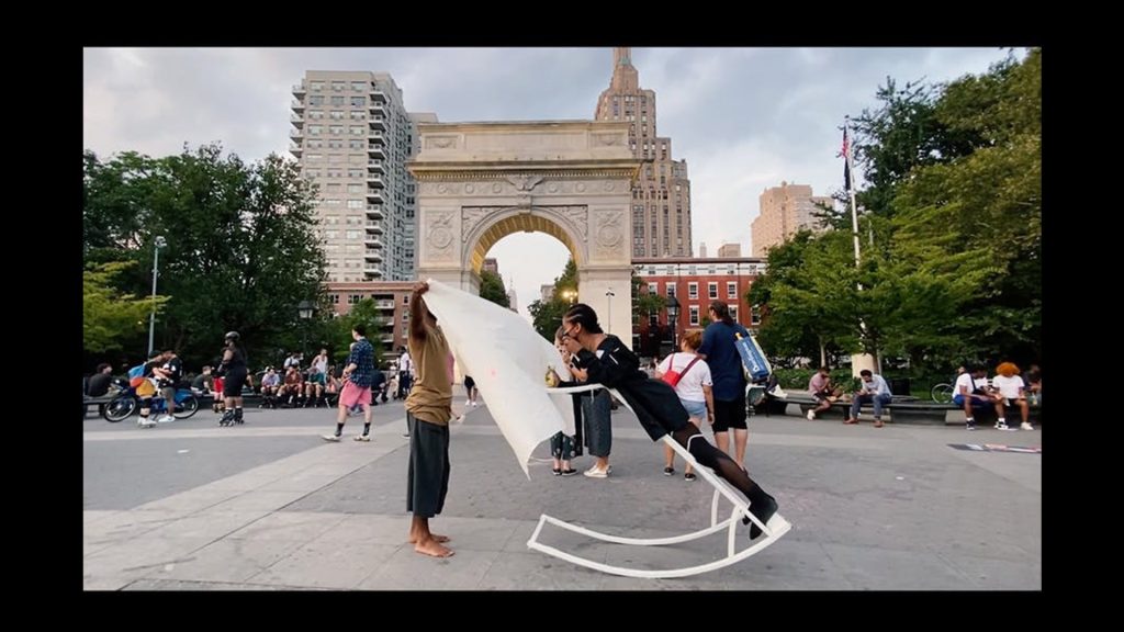 In front of the arch at Washington Square Park, Yetunde leans forward on a standing platform that rolls, painting a canvass held in front of her by a peer.